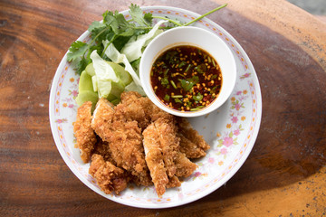 Fried chicken and a cup of sauce and salad on wood table