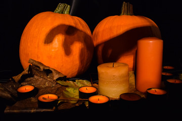 Halloween. Pumpkins, candles, autumn leaves on a black background. Scenery to celebrate Halloween.