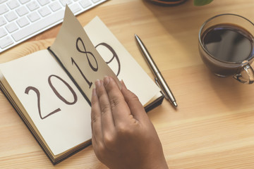 New Year 2019 is coming concept. Female hand flips notepad sheet on wooden table. 2018 is turning, 2019 is opening