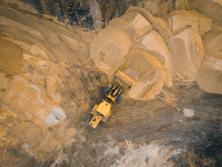 Yellow excavator or bulldozer works on construction site with sand, aerial or top view