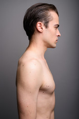 Fototapeta na wymiar Profile view of young handsome man shirtless against gray background