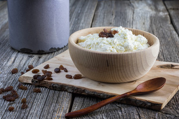 Homemade curd in a wooden bowl with raisins and wooden spoon