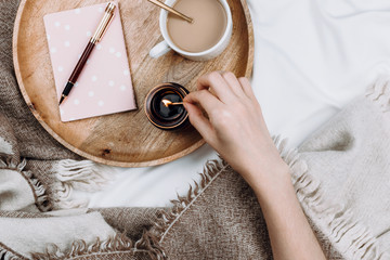 Cozy flatlay with wooden tray, cup of coffee or cocoa, candle, notebooks on white sheets and...