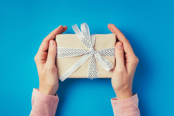 Woman's hands holding gift box on blue background, top view 