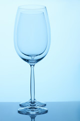 Two empty wine glasses standing together. Blue lighting.