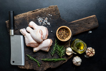 Raw uncooked chicken legs on the cutting board,meat with with salt pepper and herbs ingredients for cooking. Top view