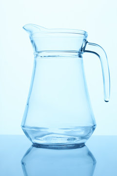 Empty clean transparent glass pitcher. Close up. Blue lighting.