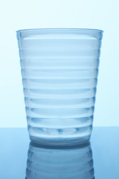 Clear Ribbed Glass Cup. Close Up. Blue Reflective Surface Background.