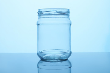Empty glass jar. Reflective surface, blue lighting.