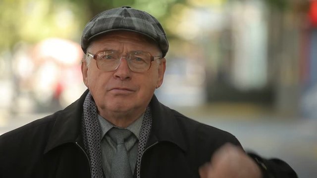  Impressive bokeh portrait of an optimistic man in a plaid flat cap and a woolen coat putting on his eyeglasses with a suprise in a street in autumn 