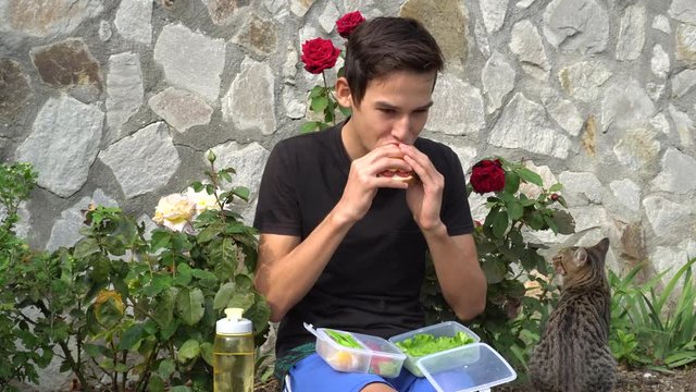 Student eating outdoors from plastick lunch boxe. Young man having a lunch break in the park