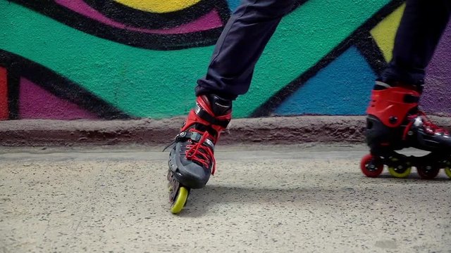 Man in rollerblades start riding near graffiti wall, focus on legs
