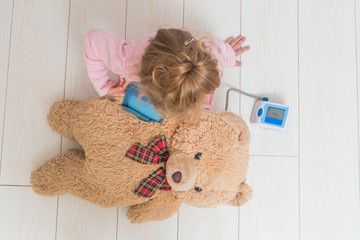 a girl, a child playing doctor, measures the pressure of a bear toy