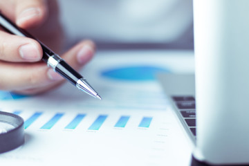 Business people use pen to point graphs to analyze company data and statistics from the chart.
