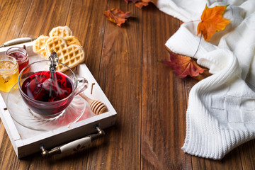 autumn fall concept with knitted blanket and hot tea with waffer, jam, honey on wooden tray on wooden background, autumn leaf . Copy space