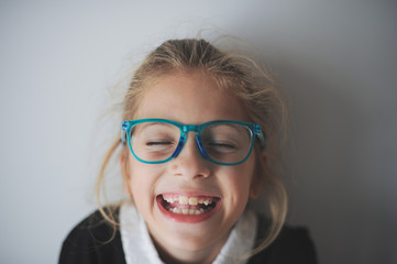 funny delightful face of little laughing caucasian girl in blue glasses