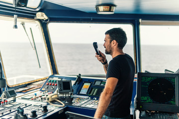 Marine navigational officer is reporting by VHF radio during navigation watch. Bridge GMDSS watch