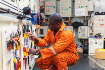 African marine engineer officer in engine control room ECR. He works in workshop and chooses...