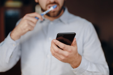 close up of man using smartphone. concept of phone addiction. young business man typing and browsing social media on his phone while brushing his teeth.