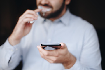 close up of man using smartphone. concept of phone addiction. young business man typing and browsing social media on his phone while brushing his teeth.