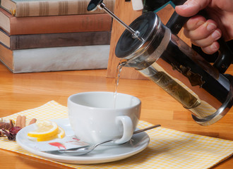 pouring herbal tea with french press teapot into white cup