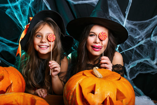 Happy Halloween. Beautiful caucasian mother and her daughter in witch costumes celebrating Halloween with Halloween candy and sweet over spider web