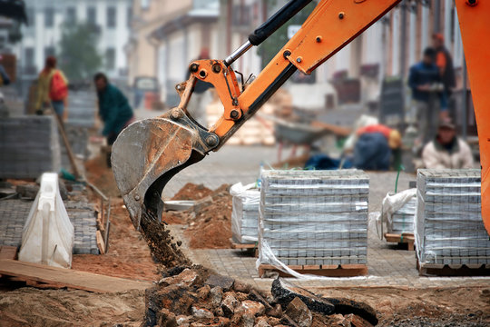 Wheel loader excavator with bucket unloading sand and pieces of asphalt at reconstruction works in the old city. Building a pedestrian street. Work on the laying of paving slabs. Heavy machinery