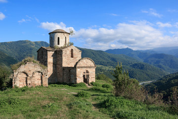 Fototapeta na wymiar Old church in mountains, in national park Dombai, Caucasus, Russia. Summer landscape, sunshine weather, dramatic blue sky and sunny day