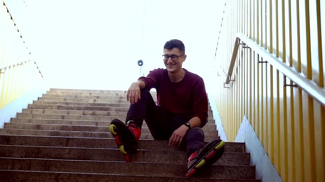 Portrait of young man with roller skate sitting on the stairs in the city super slow motion 
