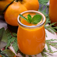 Orange smoothie topped with mint in glass jars surrounded by fruits