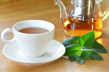 White cup and glass teapot of herbal tea with fresh mint twig on