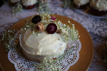 Rustic Red Velvet Wedding Cake and Cupcakes with Cream Cheese Frosting on a Gold Charger with a Doily Decorated with Dried Maroon and Pink Fall Flowers and Baby's Breath on a White Lace Tablecloth