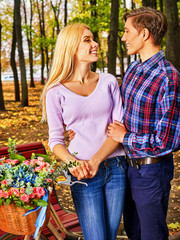 Couple bicyclein love into autumn fall park outdoor. Man and woman with flower hug under tree.