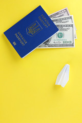 Ukrainian biometric passport and dollars. Paper plane and international passport on yellow background. Money and documents for trip abroad. Documents for immigration