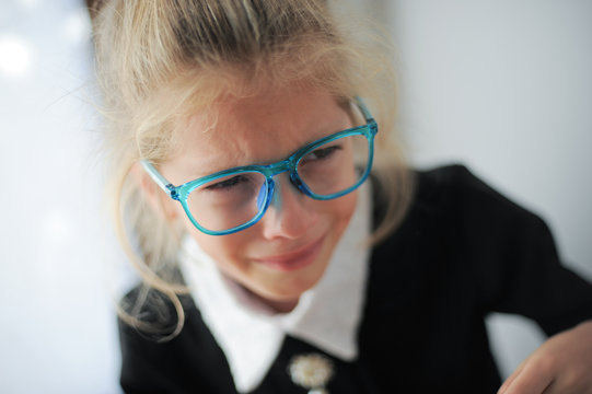 little girl in blue glasses and school black and white dress crying bitterly