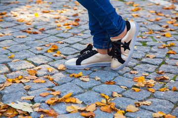 close-up of feet in jeans and sneakers on autumn Golden foliage