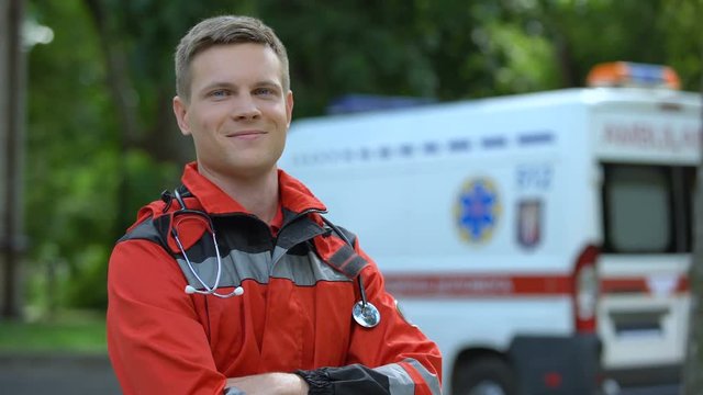 Male paramedic posing for camera, ambulance on background, professionalism