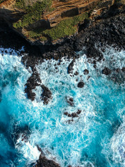 Aerial top view of sea waves hitting black volcanic rocks on the coastline with turquoise sea water. Amazing rock cliff seascape in the Portuguese coastline. Azores islands. Drone shot.