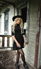 Beautiful long-legged blonde in a short black dress is standing alone near the old house