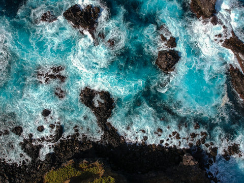 Fototapeta Aerial top view of sea waves hitting black volcanic rocks on the coastline with turquoise sea water. Amazing rock cliff seascape in the Portuguese coastline. Azores islands. Drone shot.