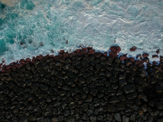 Aerial top view of sea waves hitting a stones from a jetty in pier. Drone view