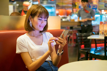 Happy Asian woman play smartphone in restaurant