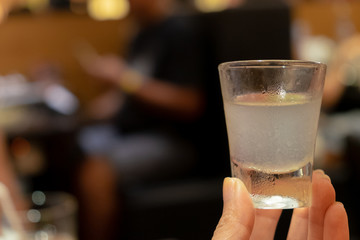 Close up hand holding lemon cocktail drink in small tumbler glass with blurry pool table background