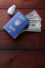 Ukrainian biometric passport and dollars. Paper plane and international passport on wooden background. Money and documents for trip abroad. Documents for immigration