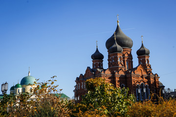 Fototapeta na wymiar The temple with red brick walls and black domes in the bright sun, near a small temple with white walls. Orthodox Christian Church in Tula, Russia