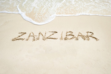 zanzibar script on light sand and ocean wave - obrazy, fototapety, plakaty