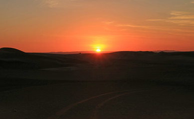 Stunning sunset over the sand dune of Huacachina desert with people and dune buggy in distance, Ica region, Peru