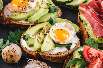 Whole grain bread sandwiches with fried quail egg, avocado, herbs and seeds on black background. Clean eating, healthy vegan breakfast