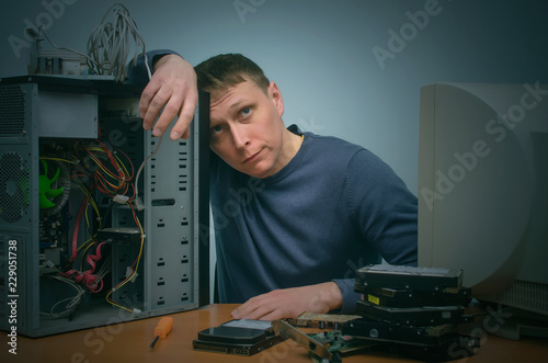 tired and bored computer repairman is sitting on his workplace and