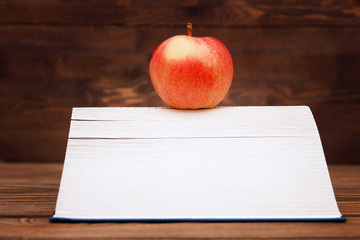 Reading book open on wooden background and red apple.